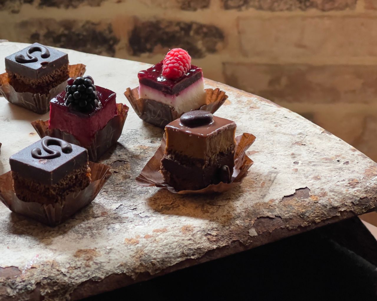 Close-up of assorted miniature desserts, highlighting chocolate and fruit garnishes on a rustic table.