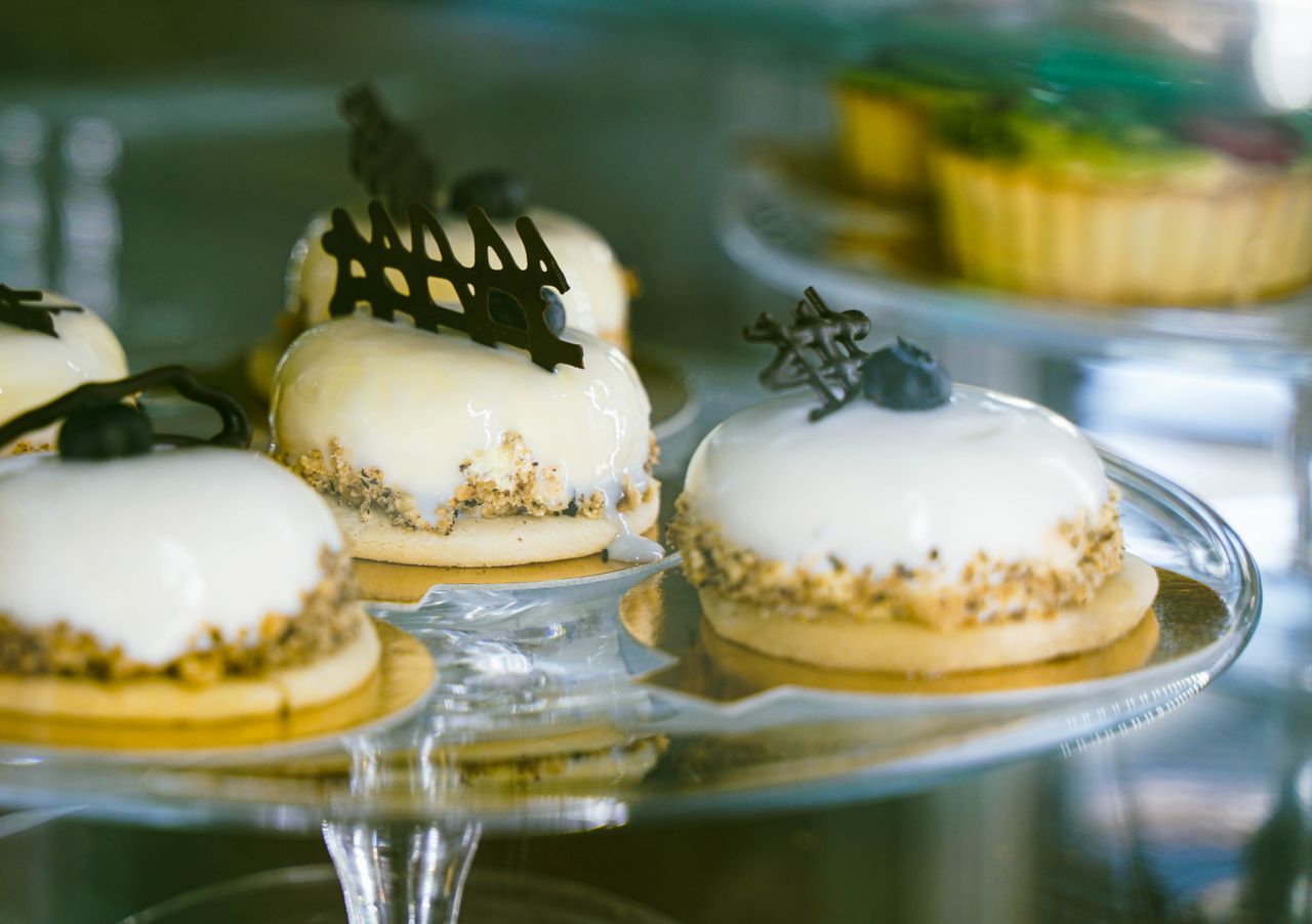 Close-up of gourmet pastries with white glaze and chocolate decor on a glass stand.